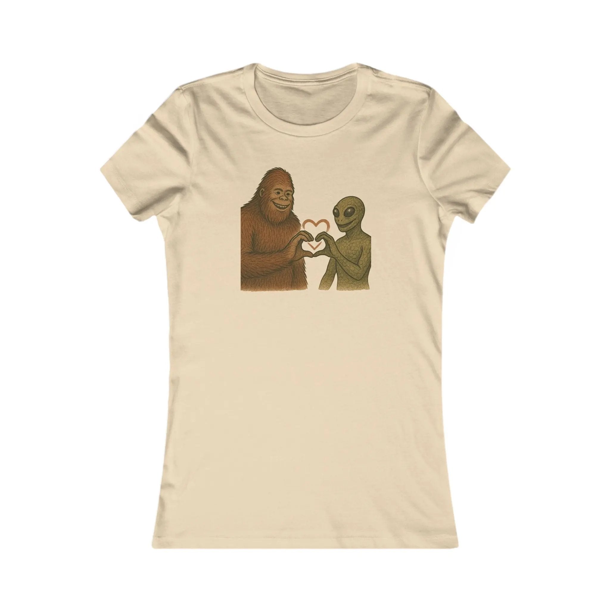 Beige t-shirt with a graphic of a bigfoot and an alien holding hands making a heart symbol on a white background