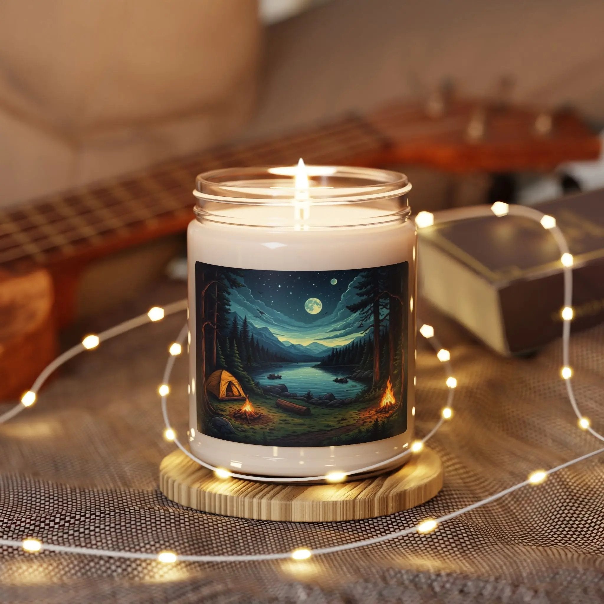 Candle with a forest design on a wooden coaster surrounded by string lights and a guitar in the background