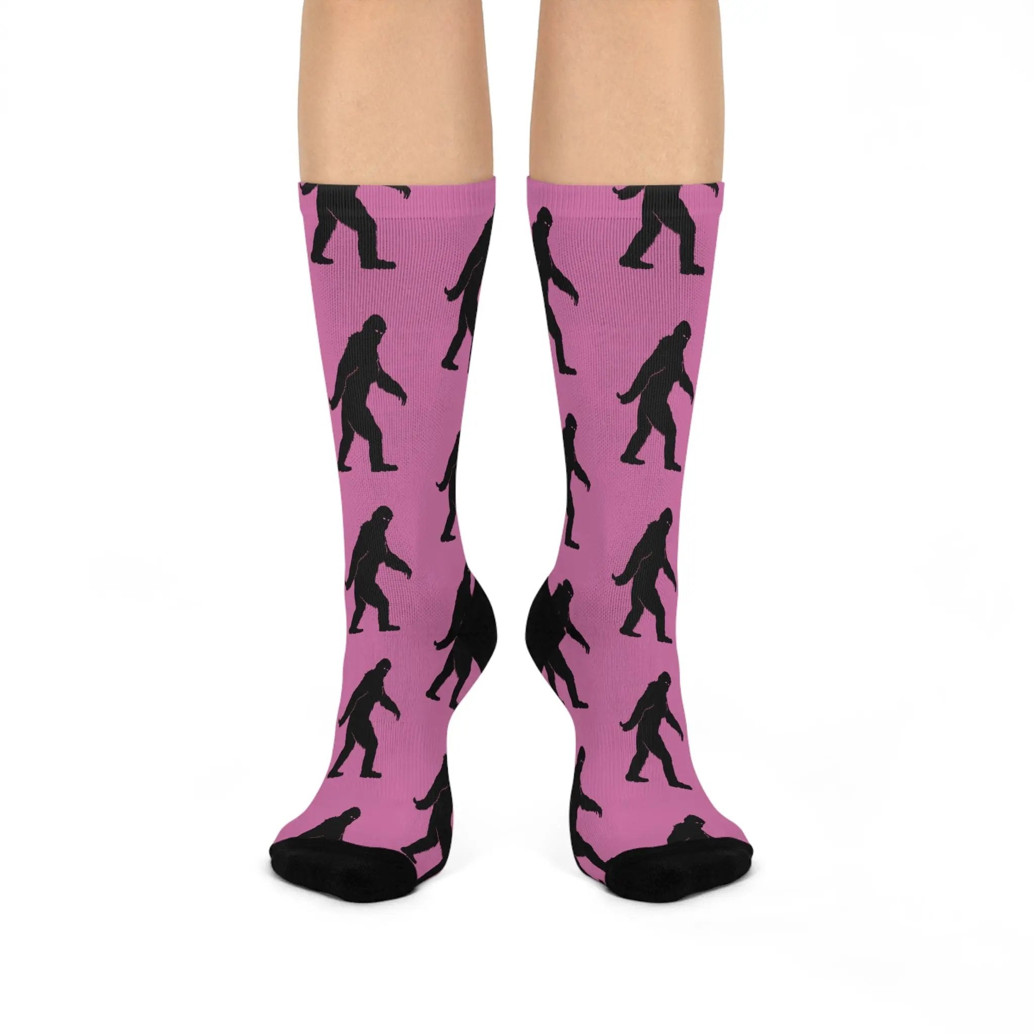 Pink socks with black Bigfoot silhouette pattern worn by a person on a white background