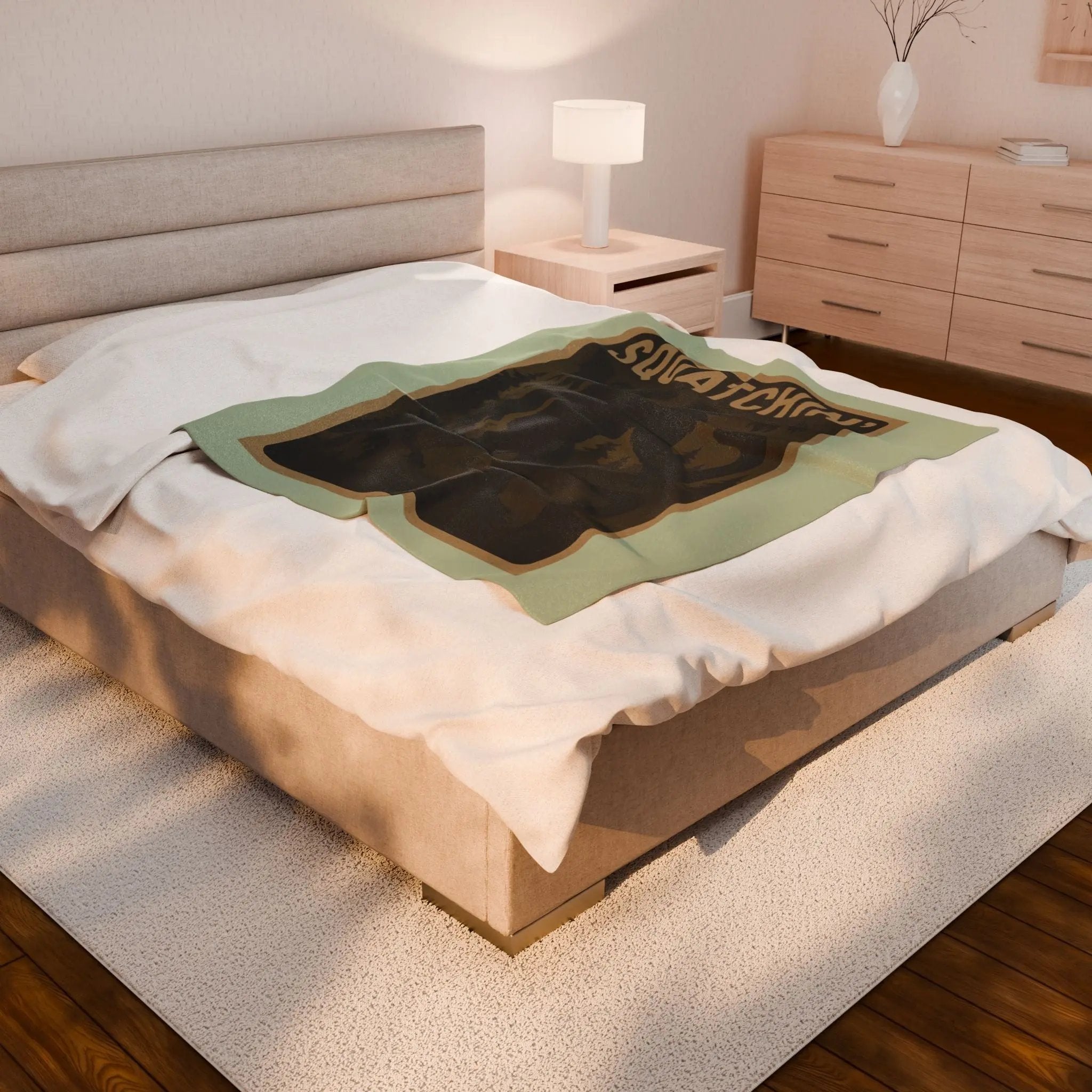 Light green fleece blanket with 'Squatchin' text across the top with silhouettes of bigfoot, loch Ness, werewolf, mothman, and an alien across a bed in a bedroom setting.