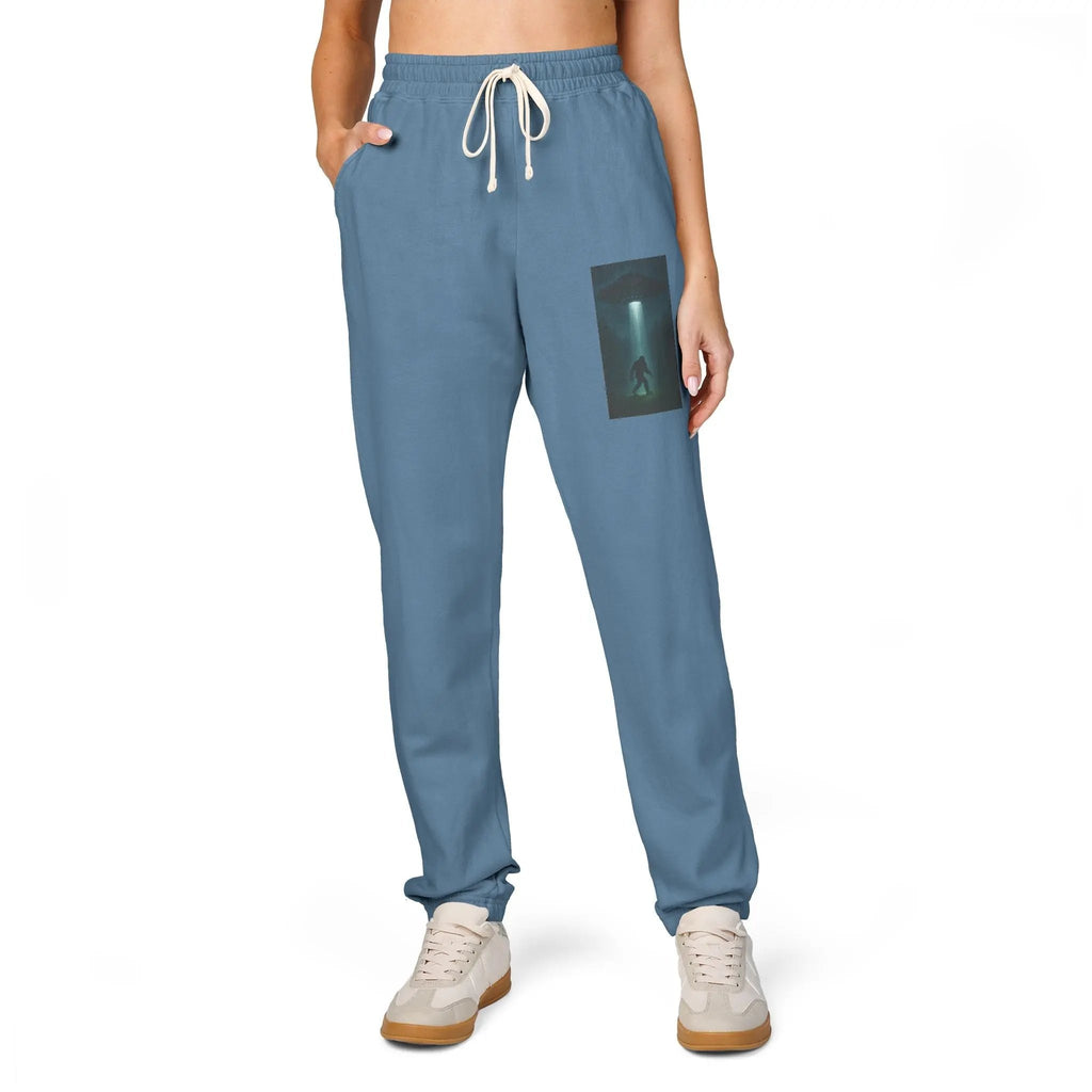 Blue sweatpants with a small graphic of a UFO with a beam of light on a bigfoot silhouette on the left leg on a white background