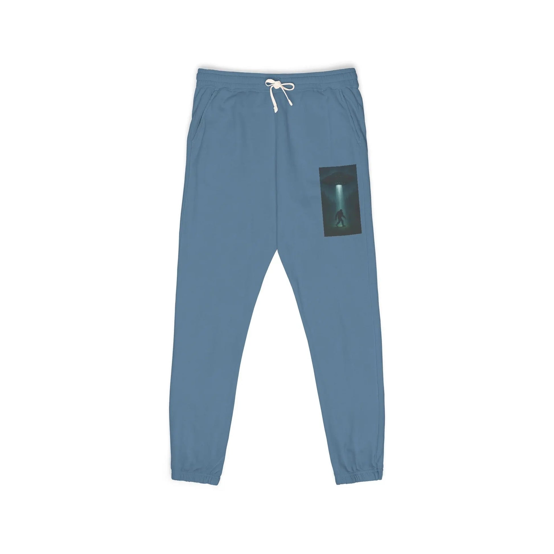 Blue sweatpants with a small graphic of a UFO with a beam of light on a bigfoot silhouette on the left leg on a white background