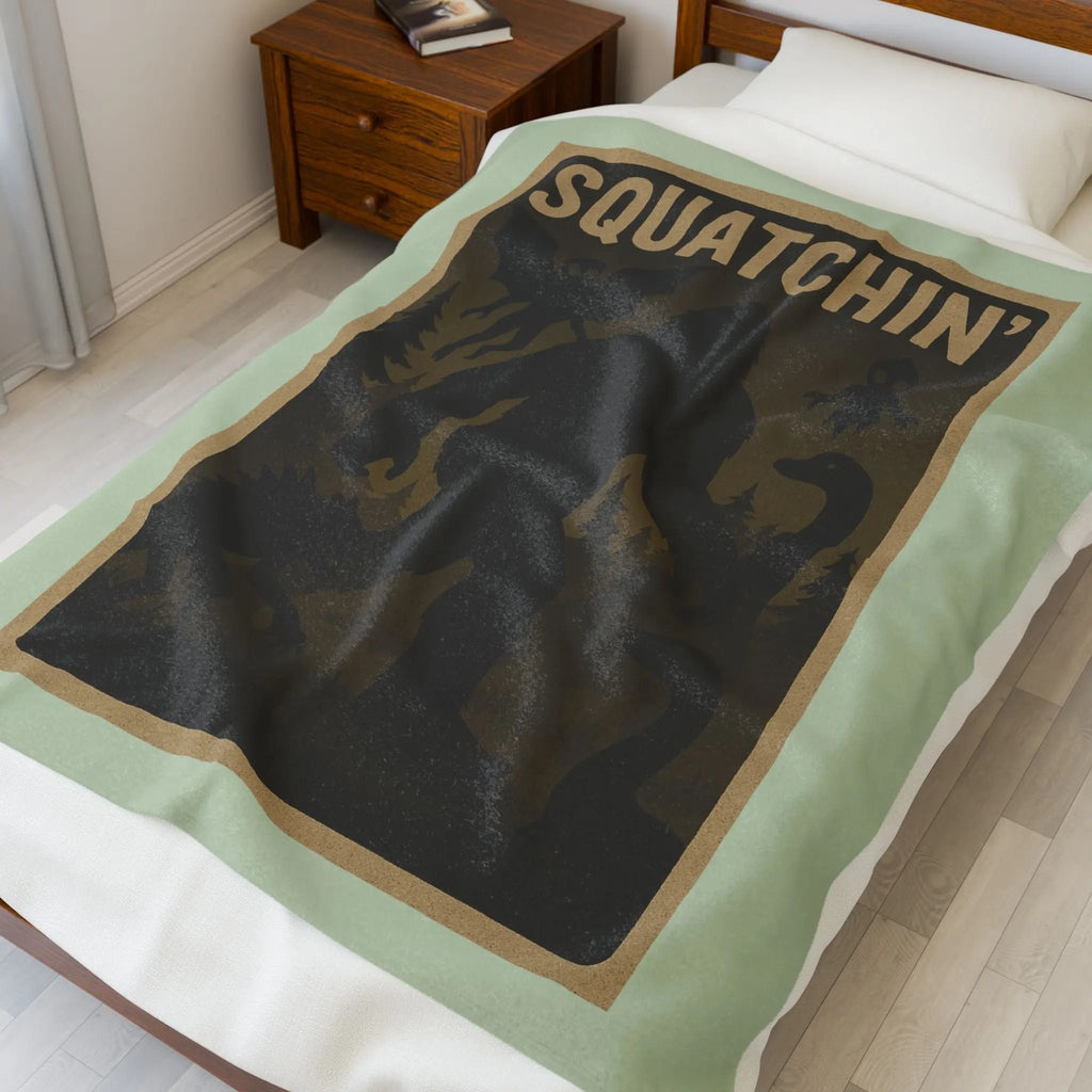 Light green fleece blanket with 'Squatchin' text across the top with silhouettes of bigfoot, loch Ness, werewolf, mothman, and an alien laying across a bed.