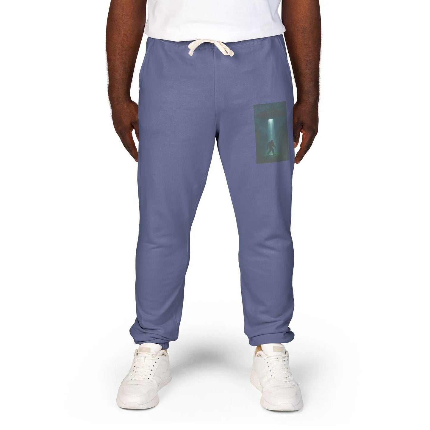 Person wearing blue jogger pants with a small graphic of a UFO with a beam of light on a bigfoot silhouette on the left leg on a white background