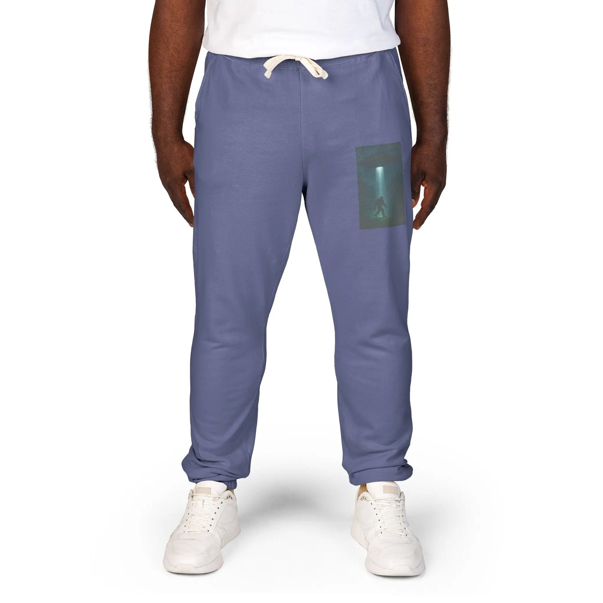Person wearing blue jogger pants with a small graphic of a UFO with a beam of light on a bigfoot silhouette on the left leg on a white background