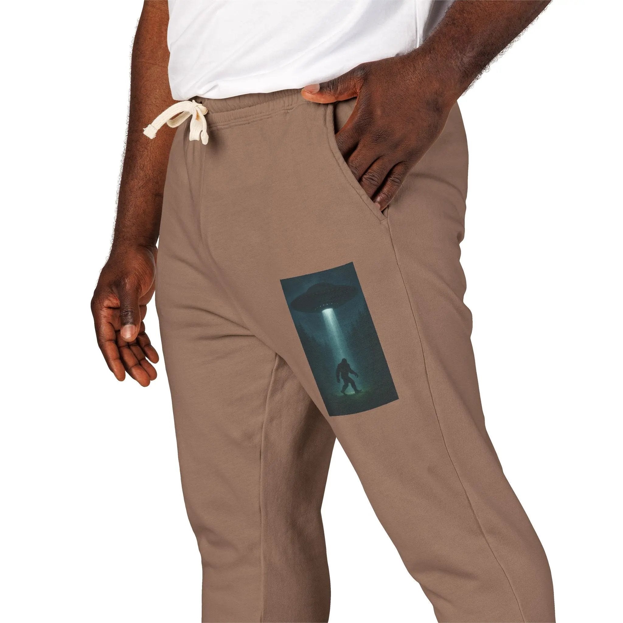 Brown pants with a small graphic of a UFO with a beam of light on a bigfoot silhouette on the left leg on a white background