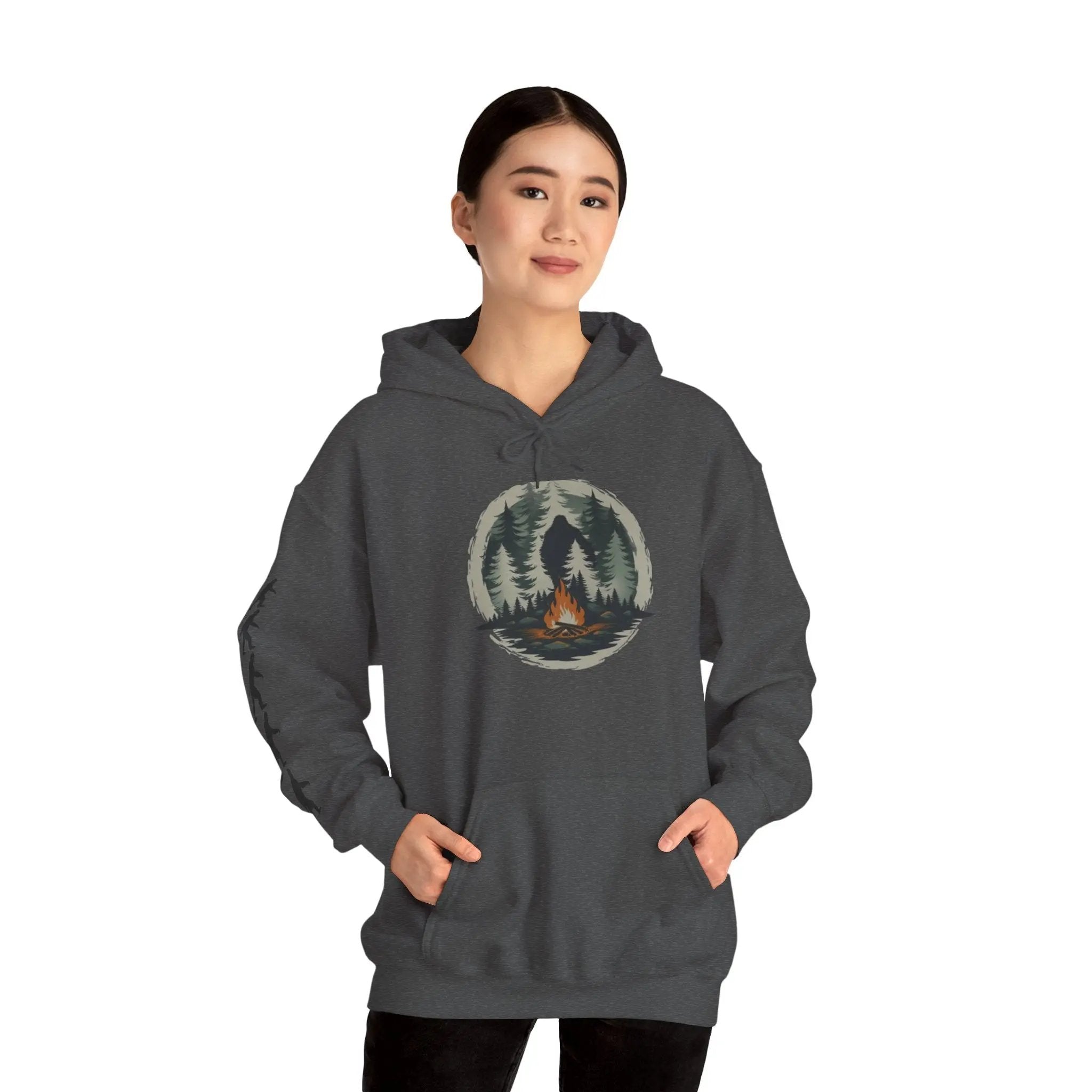 Person wearing a dark gray hoodie with a nature graphic and black bigfoot silhouettes on the right sleeve on a white background on a white background