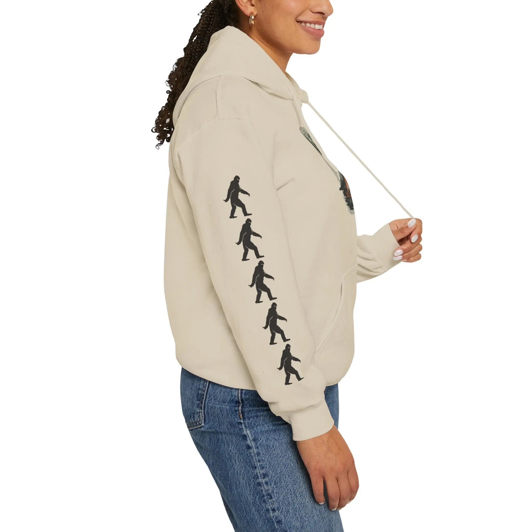 Person wearing a beige hoodie with black bigfoot graphic designs on right sleeve on a white background