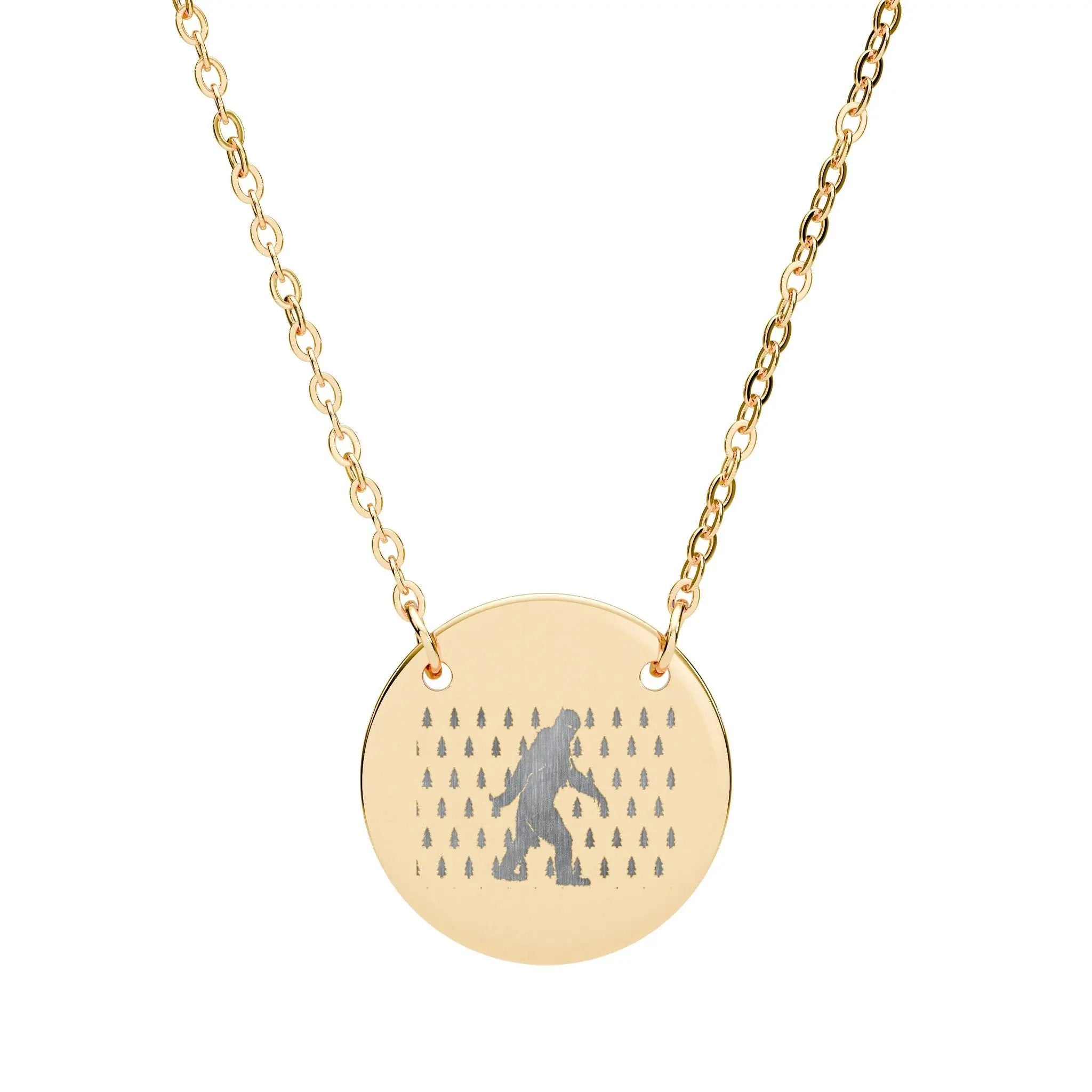 Gold necklace with a round pendant featuring a silhouette of bigfoot and small trees on a white background