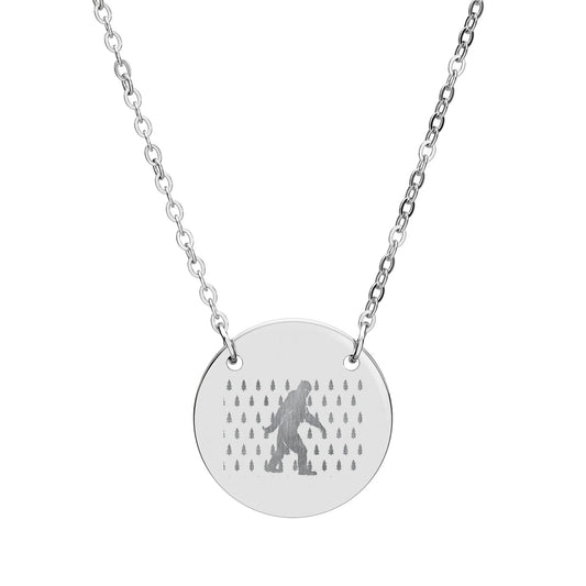Silver necklace with a round pendant featuring a silhouette of bigfoot and tree pattern on a white background