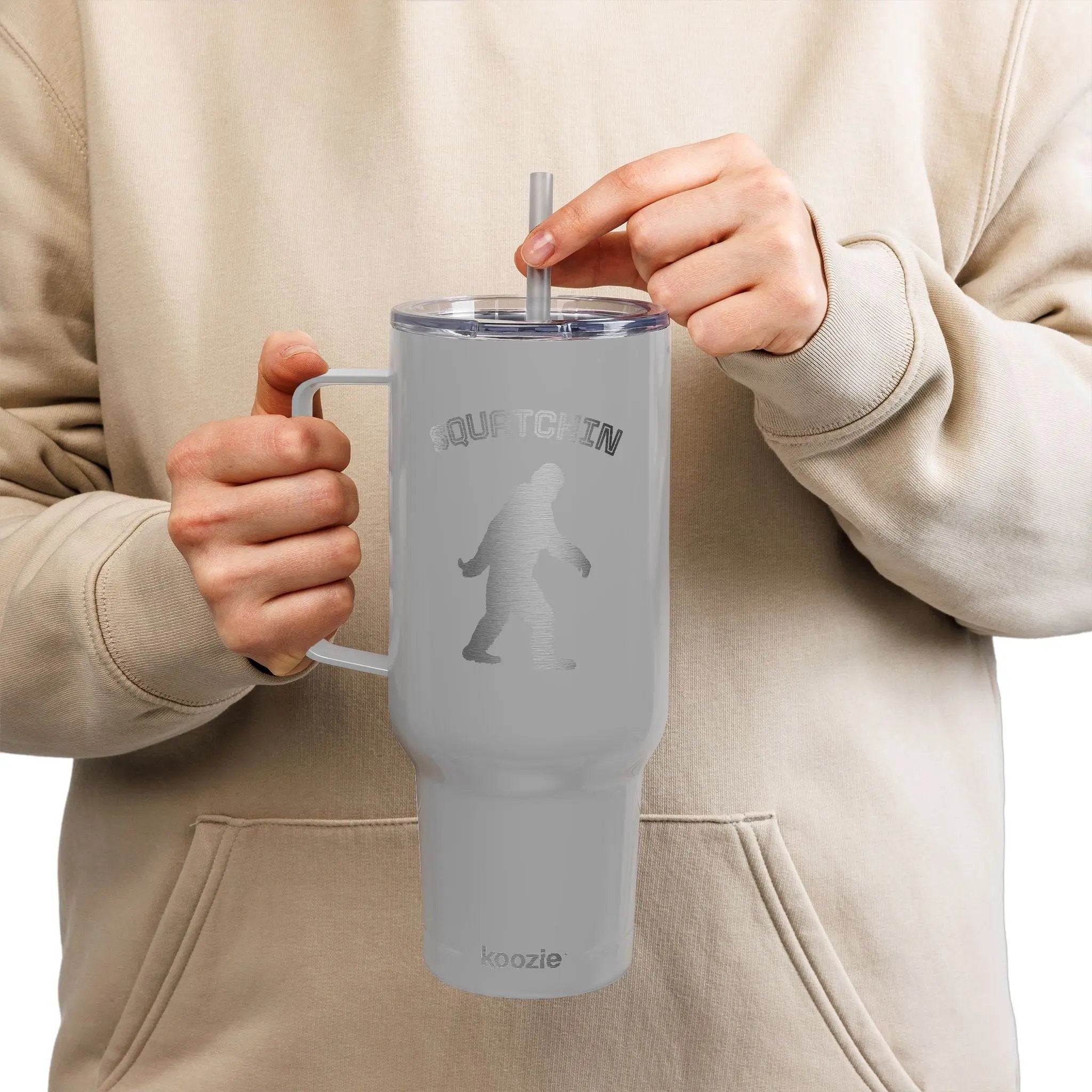 Person holding a gray tumbler with a straw, wearing a beige hoodie.