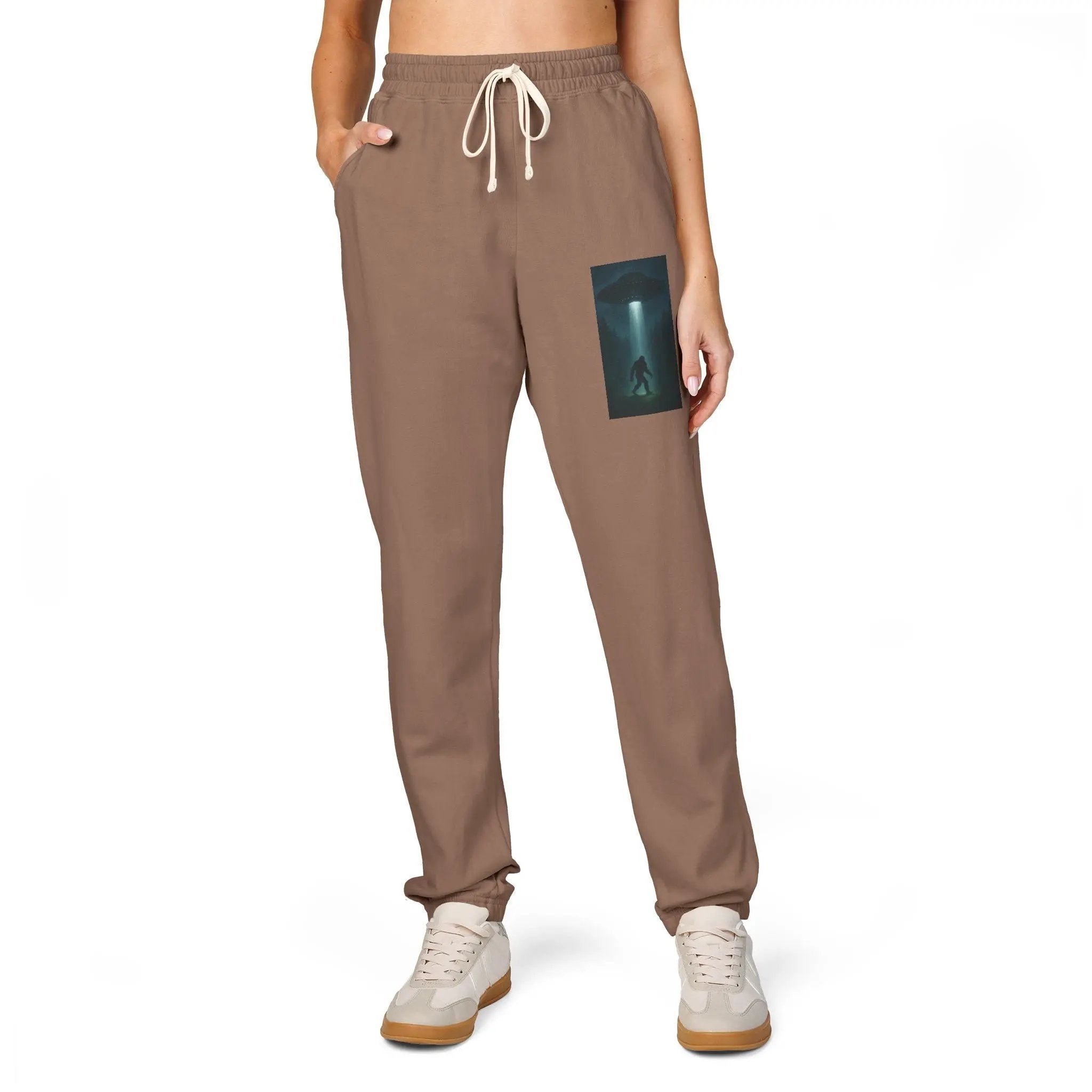 Brown sweatpants with a small graphic of a UFO with a beam of light on a bigfoot silhouette on the left leg on a white background
