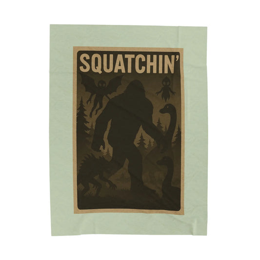 Light green fleece blanket with 'Squatchin' text across the top with silhouettes of bigfoot, loch Ness, werewolf, mothman, and an alien.