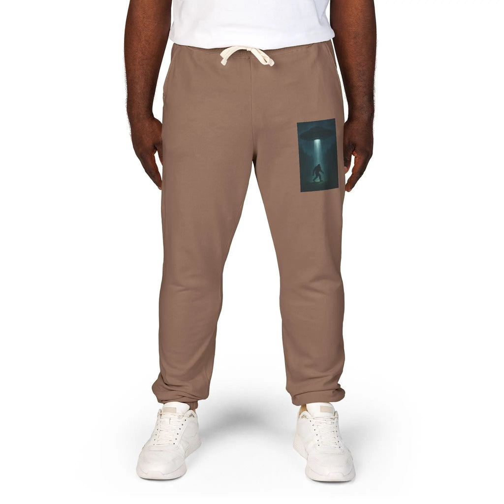 Brown jogger pants with a small graphic of a UFO with a beam of light on a bigfoot silhouette on the left leg on a white background