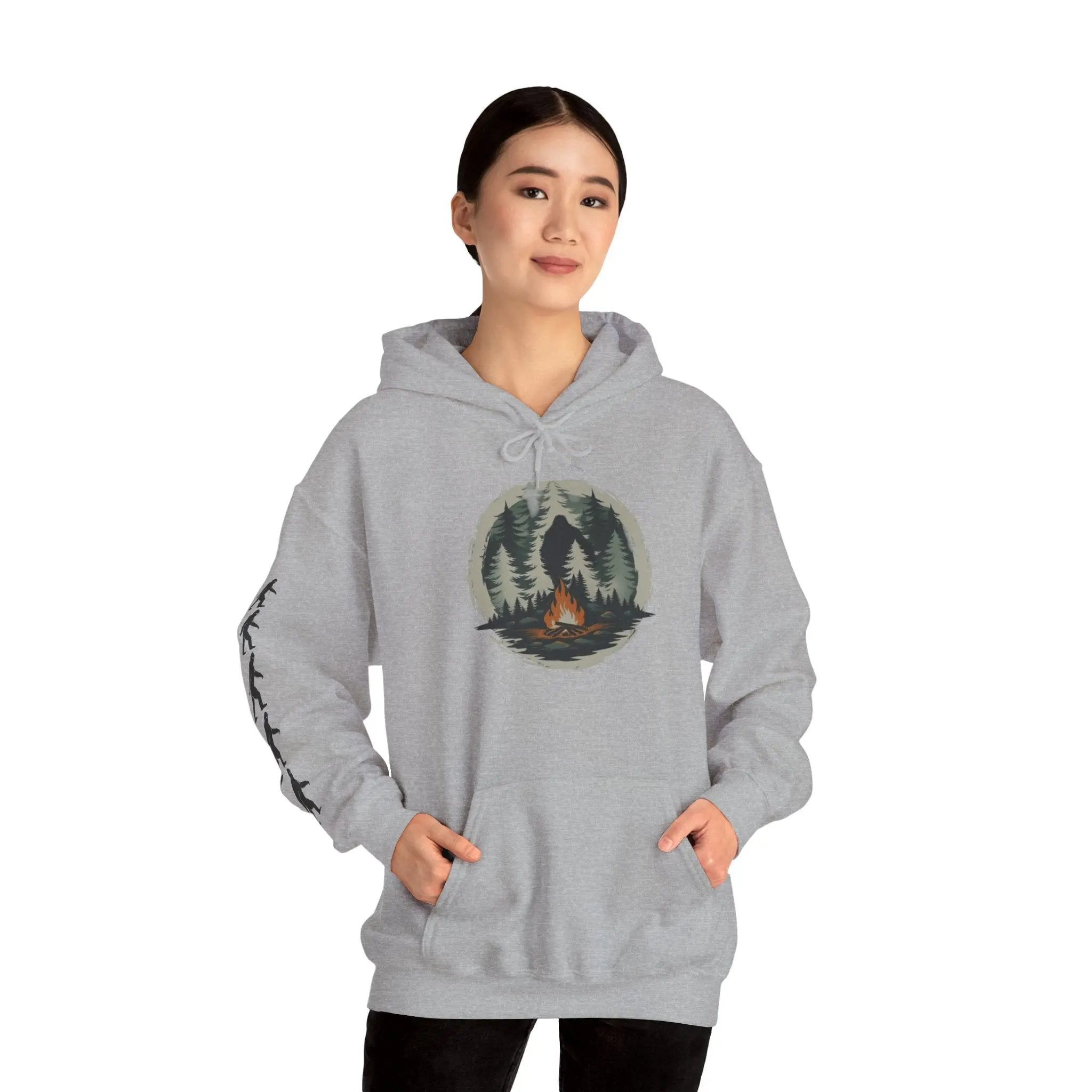 Person wearing a gray hoodie with a nature graphic and black bigfoot silhouettes on the right sleeve on a white background on a white background