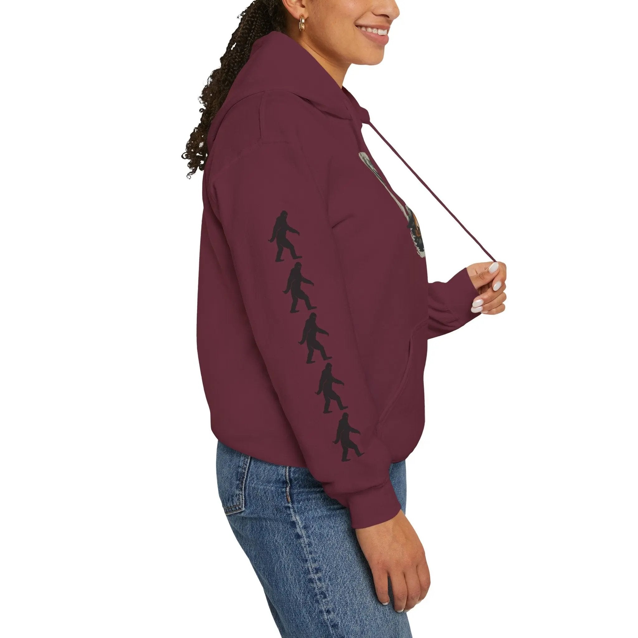 Person wearing a maroon hoodie with black bigfoot silhouette designs on right sleeve on a white background