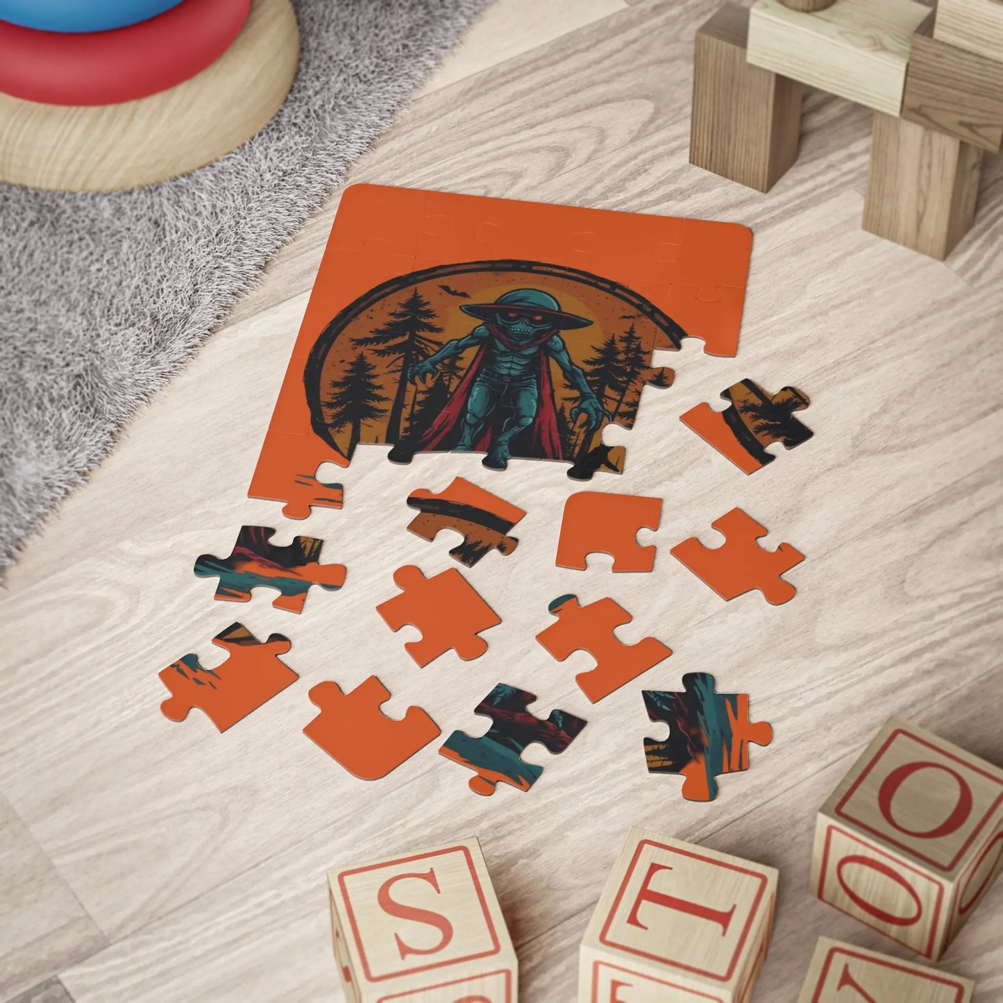 Puzzle with an alien in a cloak and nature design on an orange background, surrounded by wooden blocks on a wooden floor.