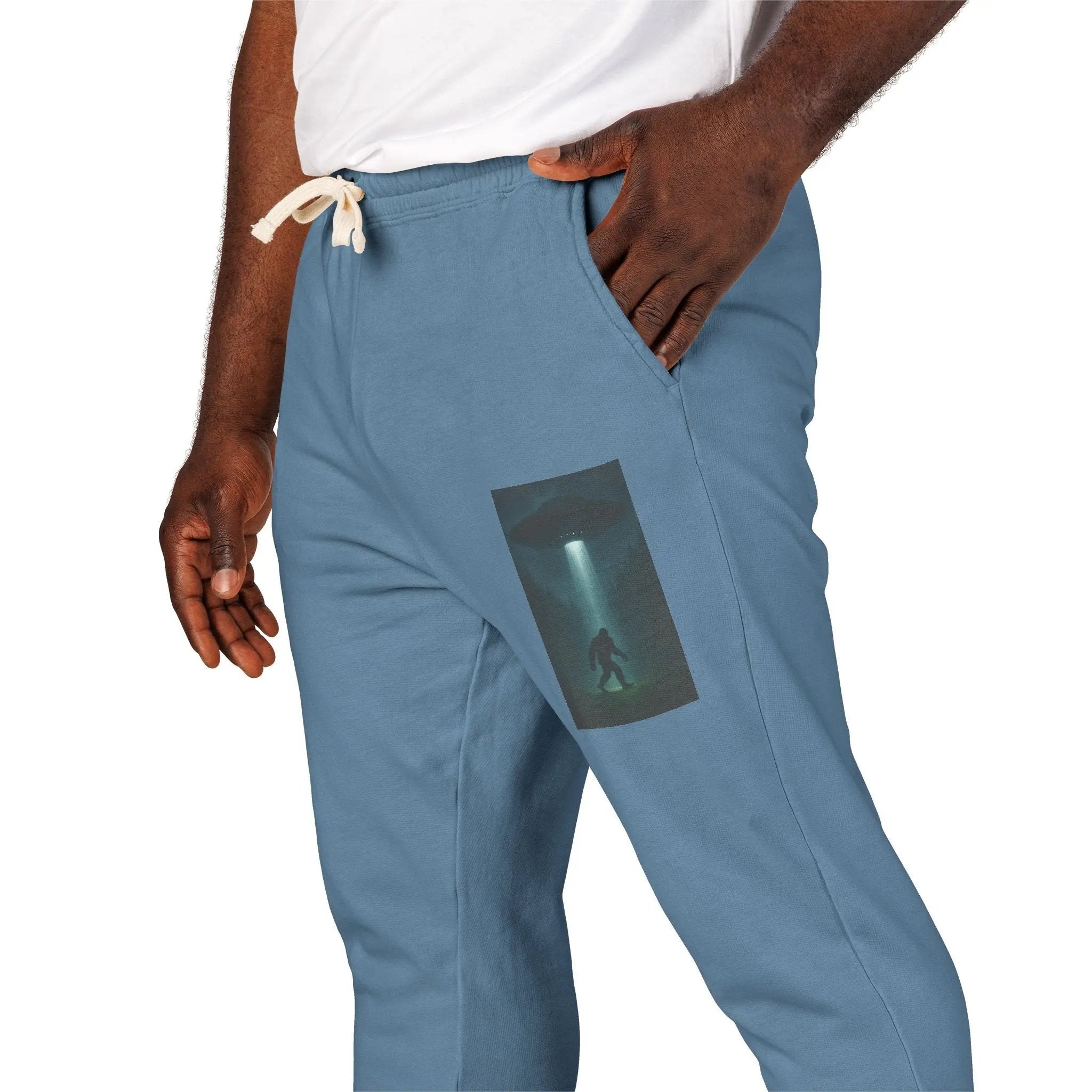 Blue jogger pants with a small graphic of a UFO with a beam of light on a bigfoot silhouette on the left leg worn by a person.