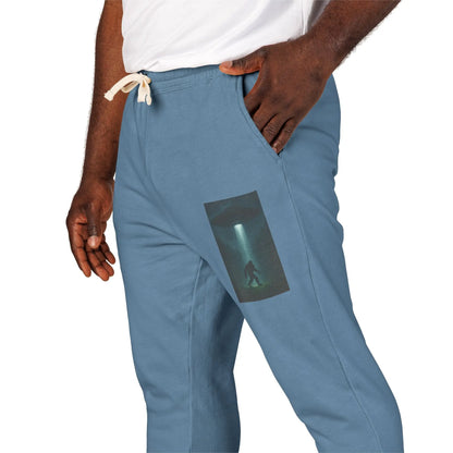 Blue jogger pants with a small graphic of a UFO with a beam of light on a bigfoot silhouette on the left leg worn by a person.
